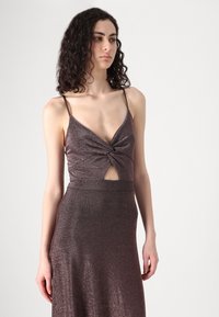 Rochie strălucitoare, de culoare mov închis, cu un corset ajustat, detaliu nodat în față și o decupare. Siluetă cu fustă lungă. Bretele subțiri, ajustabile, în stil spaghetti.