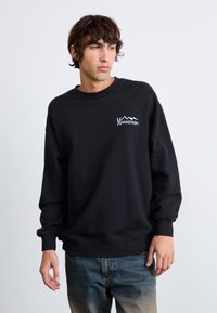 Black sweatshirt made of cotton blend, featuring a crew neck, ribbed cuffs, and a white logo with mountain design on the chest.