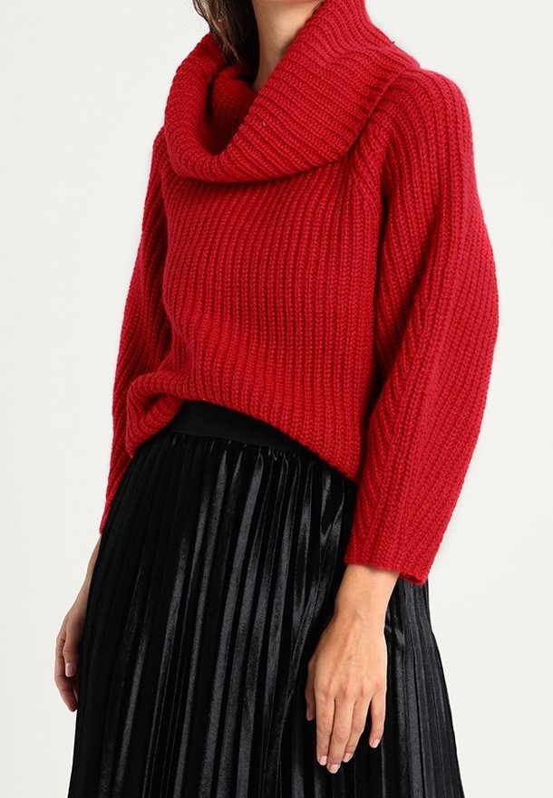 Rode gebreide trui met een col-nek, geribbelde textuur en driekwart mouwen, gecombineerd met een zwarte geplooide rok.
