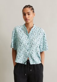 Short-sleeve button-up shirt in light blue fabric with a pattern of abstract shapes and black accents. Casual fit with a notched collar.