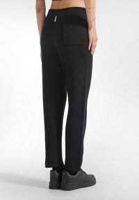 Zwarte tapering broek van gestructureerde stof, met een elastische tailleband en een enkele achterzak, gecombineerd met zwarte sneakers.
