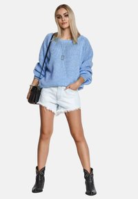Jasnoniebieski sweter dzianinowy o luźnym kroju, zestawiony z przetartymi szortami dżinsowymi i czarnymi botkami za kostkę z ćwiekami. Srebrny naszyjnik dodaje szczegółu.