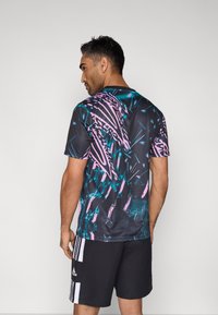 Kortærmet træningstrøje med et flerfarvet abstrakt mønster i sort, grønblå og pink. Har en rund halsudskæring og en glat tekstur.