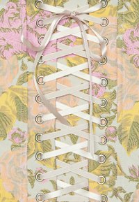 Corset en tissu floral avec des roses roses, jaunes et vertes, lacé avec un ruban de satin blanc passant à travers des œillets métalliques.
