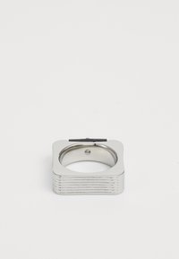Square silver metal ring with rounded edges and a ribbed texture on the sides, against a plain white background.