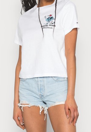 Biała bawełniana koszulka z logo Tommy Jeans i grafiką, w połączeniu z jasnoniebieskimi spodniami dżinsowymi z przetarciami.