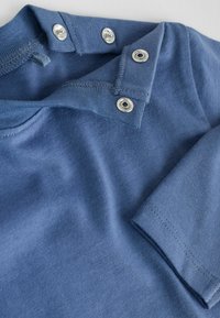 Blauwe katoenen polo met twee drukknoopsluitingen bij de kraag, korte mouwen en een zachte, gestructureerde afwerking.