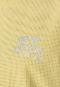 Tejido texturizado amarillo con un patrón de cuadrícula y una impresión gráfica en plata que dice "KARMA89."