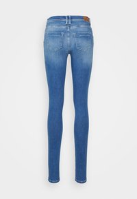 Jeans skinny em um tom azul médio, com uma cintura alta, design de cinco bolsos e desbotamento suave em direção aos tornozelos.
