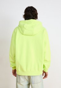 Neon grön huvtröja med en stor huva, lös passform, ribbad nederdel och muddar. Mjuk textur; enkel design utan synliga logotyper eller mönster.