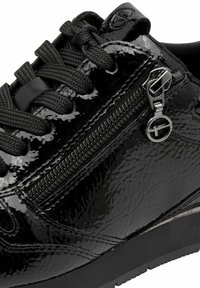 Svart lackläder sneaker med texturerad yta, rund tå, svarta snören och sidodetalj med dragkedja samt metallisk accent.