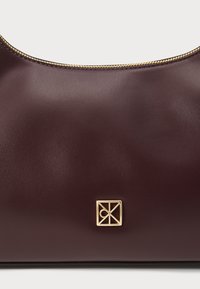 Burgundska kožna torba na rame s glatkom teksturom, s zlatnim patentnim zatvaračem i kvadratnim logom na prednjoj strani.
