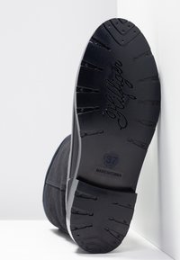 Musta kumipohja, jossa on syvät uritetut kuvioinnit, esillä kohokuvioitu tuotemerkki "Hilfiger" ja kokoluku "37", valkoisella taustalla.