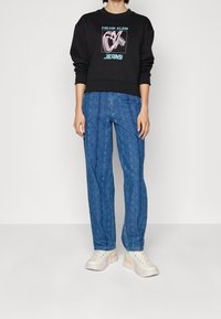 Černá mikina s grafickým potiskem, v kombinaci se světle modrými vzorovanými kalhotami. Oblečeno s bílými teniskami s pastelovými akcenty.