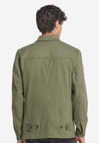 Olivgrön, lätt jacka med rak skärning, knäppta manschetter och baksidesdetaljer med två knappar för justering.