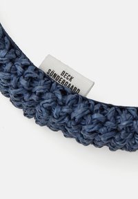 Megzta tamsiai mėlyna galvos juosta su tekstūruotu raštu, išskirtiniu baltu etikete, ant kurios juodu spaudu u�žrašyta "BECK SØNDERGAARD".