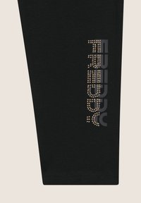 Leggings neri con una grafica di borchie metalliche sulla gamba sinistra, con una texture liscia e un design aderente.