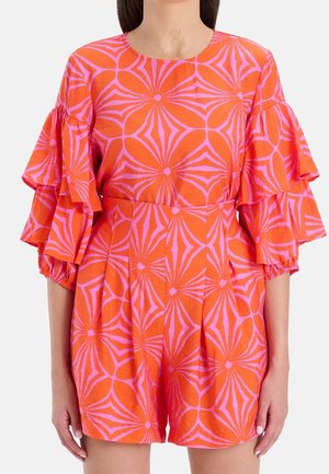 Vrouw draagt een feloranje en roze jurk met een geometrisch patroon, gelaagde ruches aan de mouwen en een ronde halslijn.