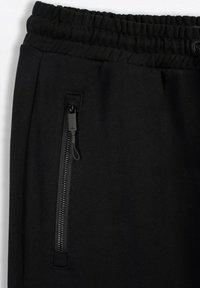 Czarne dresy z elastycznym pasem, regulowanym sznurkiem i boczną kieszenią zapinaną na zamek błyskawiczny w kolorze czarnym z uchwytem.