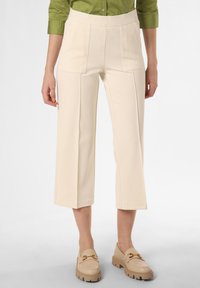 Béžové zkrácené kalhoty s předními kapsami, texturovaná tkanina a široké nohavice. Vybavené světlými mokasíny se zlatými akcenty.