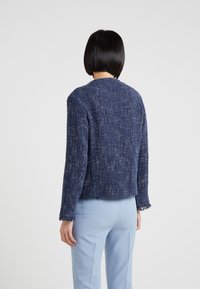 Merenneitokankainen bleiseri karkealla kankaalla, lyhennetty muotoilu ja rispaantunut helma. Yhdistetty vaaleansinisiin housuihin.