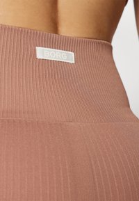 Ribbed, hoch taillierte Leggings in staubigem Rosé mit einem weißen "BORG"-Label auf der Rückseite. Das Material wirkt dehnbar und glatt.