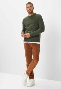 Grüner Strickpullover mit gerippter Struktur, braune Cordhosen und weiße Sneakers. Schlichtes Rundhalsdesign, taillierte Passform und gerader Beinabschluss.