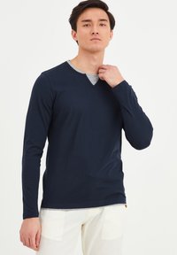 Marineblå langærmet t-shirt med V-hals design. Fremstillet af blødt stof, med en grå kant ved kraven. Pasformen er afslappet.