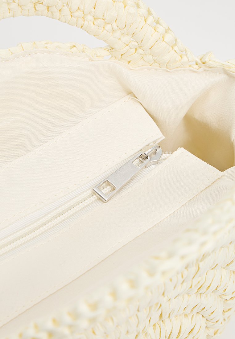 Bolso de mano de paja trenzada en amarillo claro con exterior texturizado; el interior cuenta con un forro de tela beige y un compartimento con cierre.