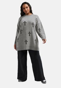 Grå stickad tröja med ett korsmönster i svart, med ribbade muddlar och fåll. Matcher med löst sittande svarta byxor och träningsskor.