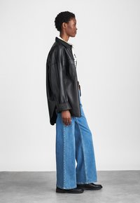 Veste en cuir noir surdimensionnée, jeans en denim bleu clair larges et bottines noires. La veste présente de grandes poches et des poignets larges.