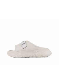 Chaussure blanche à enfiler avec une semelle en caoutchouc texturé, large sangle et un design embossé subtil. Équipée d'une sangle réglable grise pour un ajustement parfait.