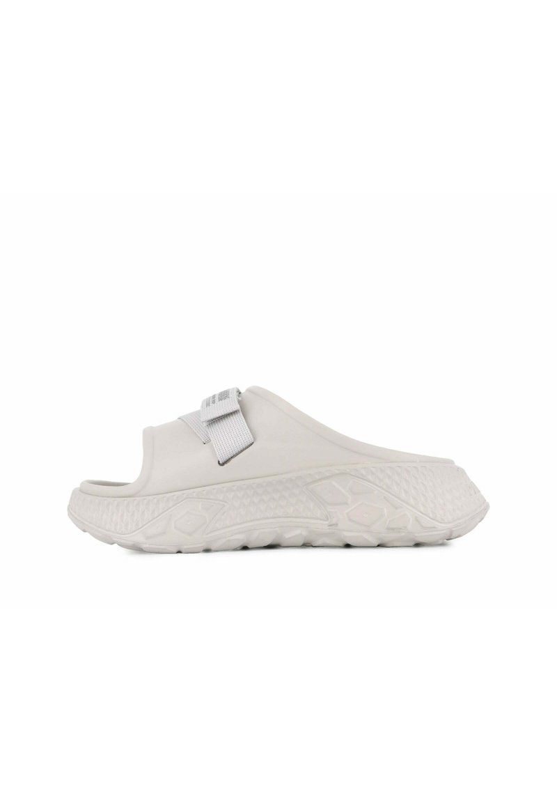 Chaussure blanche à enfiler avec une semelle en caoutchouc texturé, large sangle et un design embossé subtil. Équipée d'une sangle réglable grise pour un ajustement parfait.