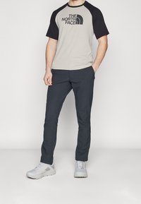 Camiseta raglán de manga corta en gris y negro con logo, combinada con pantalones oscuros y zapatillas deportivas gris claro con suelas texturizadas.