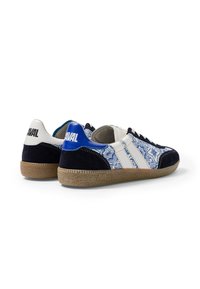 Paire de baskets basses avec tissu bleu et blanc à motifs, bandes en cuir blanc, accents en daim noir et semelles en caoutchouc brun texturées.