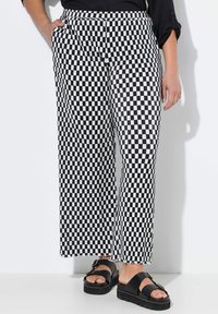 Pantalons larges à carreaux noirs et blancs avec taille élastique et poches latérales, associés à des sandales à plateforme noires.