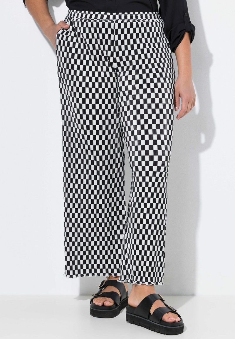 Pantalons larges à carreaux noirs et blancs avec taille élastique et poches latérales, associés à des sandales à plateforme noires.