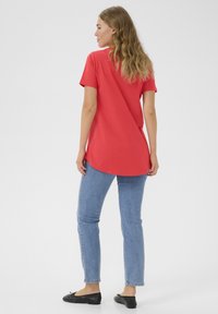 Red cotton t-shirt with short sleeves, curved hem, paired with light blue slim-fit jeans and black flat shoes.
