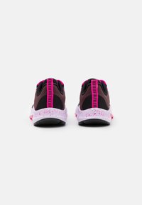 Un par de zapatillas deportivas en negro y morado oscuro con acentos en rosa brillante y suelas blancas, vistas desde atrás sobre un fondo blanco.