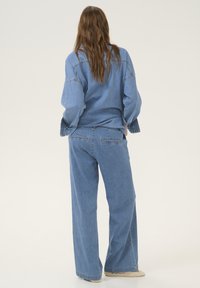 Denim odjeća koja se sastoji od lagane, široke svijetloplave košulje i hlača širokih nogavica. Tkanina je mekana s minimalnim detaljima šivanja i džepovima.