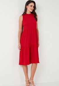 Red sleeveless dress with a round neckline, tiered design, and a flowing silhouette. Made from lightweight fabric, finished at mid-calf.
