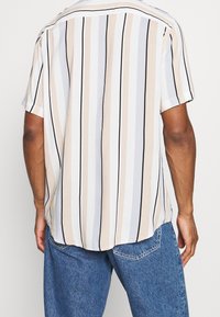 Camicia a manica corta con bottoni e righe verticali in beige, crema e blu. Tessuto leggero, orlo dritto e spacchi laterali.