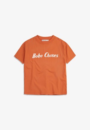 Camiseta naranja de manga corta de algodón con texto blanco "Bobo Choses" impreso en el pecho, cuello redondo y etiqueta visible de la marca en el interior del cuello.