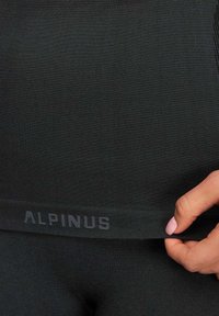 Czarne legginsy o fakturowanym wykończeniu, z szerokim pasem w kolorze szarym z napisem "ALPINUS". Materiał wydaje się elastyczny i dopasowany.