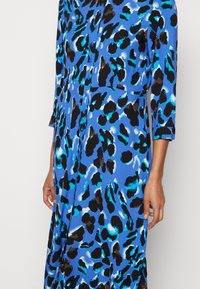 Blaues Kleid mit Leopardenmuster, dreiviertellangen Ärmeln, Knopfleiste vorne und lockerem Schnitt. Mit schwarzen und türkisfarbenen Akzenten. Weiche Stofftextur.