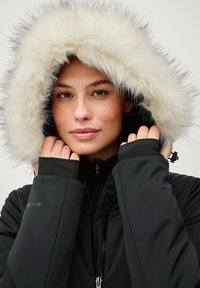 Sort vinterjakke med en hætte foret med kunstpels. Har en frontlynlås og tætsiddende manchetter, der giver varme og komfort.