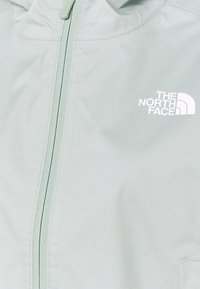 Chaqueta de cremallera verde claro hecha de tejido suave, con cremallera frontal y el logo blanco de "The North Face" en el pecho.