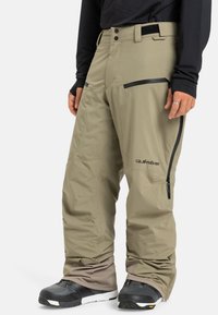 Pantalons de neige beiges avec une coupe décontractée, dotés de poches zippées, d'une taille ajustable et de bas de pantalon renforcés. Fabriqués en matériau durable et résistant à l'eau.