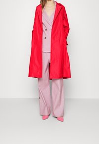 Cienki czerwony płaszcz przeciwdeszczowy z kapturem, w połączeniu z jasnoróżowym, teksturowanym garniturem i pasującymi różowymi butami. Posiada zapinaną marynarkę oraz spodnie o szerokich nogawkach.