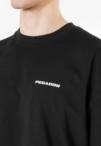 Zwarte katoenen t-shirt met een ronde hals, voorzien van een klein wit "PEGADOR" logo op de borst, met een soepele textuur en een ontspannen pasvorm.